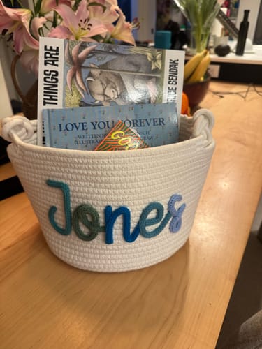 Customer's medium personalized knitted basket with the name 'Jones' in multicolor yarn, holding several children's books.