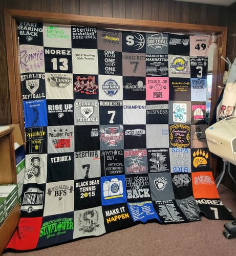 Customer's finished Premium T Shirt Quilt with various school shirts hanging up indoors.