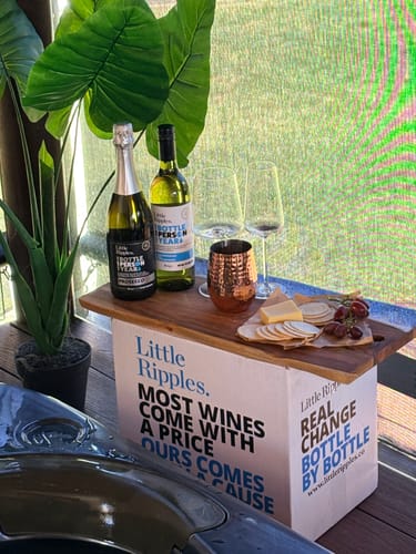 Reviewer's bottle of Sauvignon Blanc and Prosecco set up outdoors with glasses and a cheese board on a branded box.