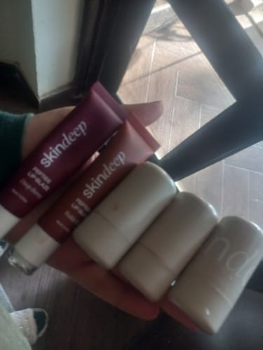 Customer's hand holding a collection of skindeep products, including a dark pink Peptide Lip Glaze tube.