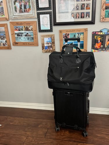 Reviewer's black Nobl luggage set, with a duffel bag stacked on a rolling suitcase indoors.