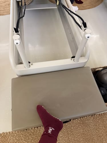 Customer's foot in a sock rests near their white Pilates Lover machine.