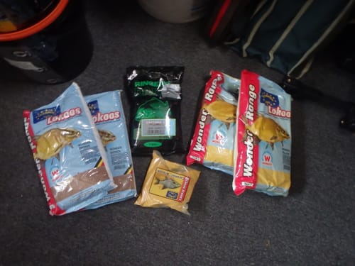 Recensent toont twee zakken Wonder Range Yellow lokaas, uitgestald op de vloer naast ander visvoer.