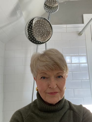 Reviewer with her newly installed chrome Dual Shower Head Set in a white-tiled shower.