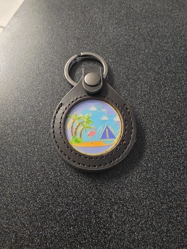 Customer's dark brown leather keychain holder displaying a colorful sobriety coin with a beach scene inside.