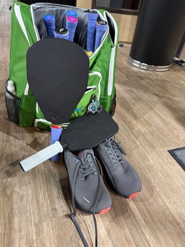 Customer's grey MUUV Stride pickleball shoes on a floor with a pickleball bag and paddles.