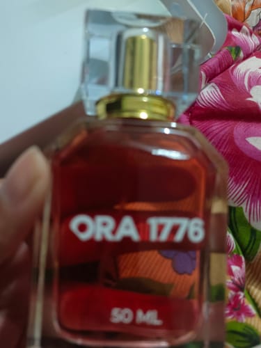 Close-up: Customer holding the clear bottle of Ora 1776 perfume, showing the reddish liquid.