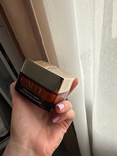 Reviewer's hand holding the Youth Elixir anti-wrinkle face cream in its square, amber jar.