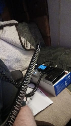 Kunde zeigt seinen neuen Gitarren-Modeler mit eingeschaltetem Display neben seiner E-Gitarre.