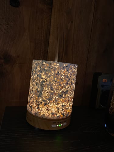 Recensentfoto van een verlichte aromadiffuser die een warme gloed geeft in een donkere kamer.