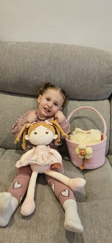 Reviewer's child smiling on a couch with the doll and pink basket from the Personalized Love Basket set.