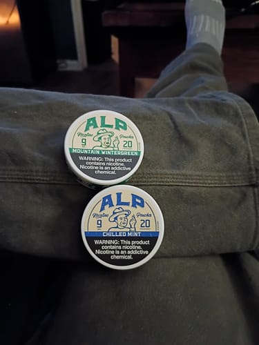 Customer's tins of ALP Chilled Mint and Mountain Wintergreen nicotine pouches resting on their lap.
