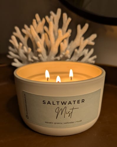 Reviewer's lit Saltwater Mist Candle with three wicks burning in a cozy, decorative setting.