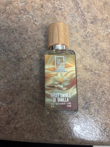 Customer's bottle of Misty Swirls Of Vanilla perfume with a wooden cap, sitting on a stone countertop.