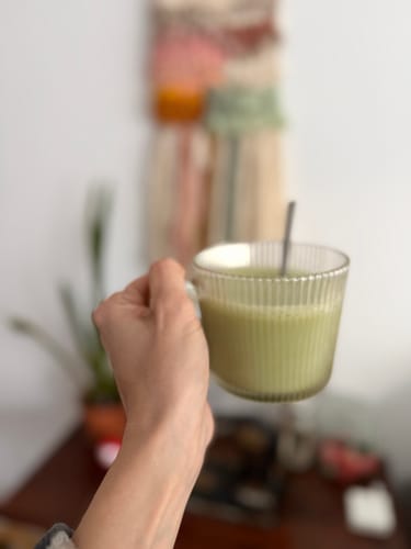 Primer plano de un cliente sosteniendo una taza de cristal con Té Matcha Premium Coco.