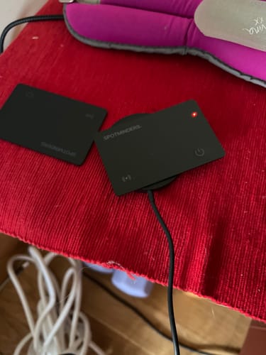 Customer's black SPOTMINDERS wireless charger plugged in on a red surface, with its red power light on.