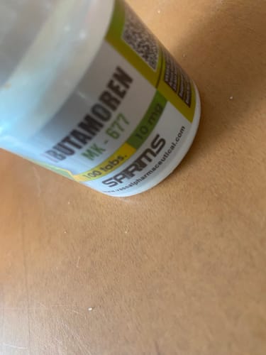 Primer plano del frasco de Ibutamoren (MK-677) de un cliente sobre una mesa de madera.