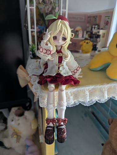 Reviewer's adorable AnYao action figure sitting on a shelf. The blonde doll wears a red and white outfit and makes a peace sign.