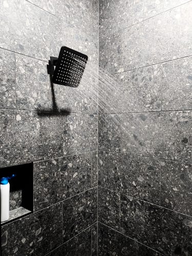 Customer's black Square Rain Shower Head installed in a tiled shower, spraying a full stream of water.
