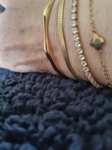 Close-up of a reviewer's wrist wearing the gold Bamboo Bangle stacked with several other bracelets.