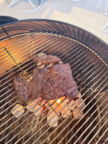 Customer grilling a thick ribeye steak from the Quarter Beef Bundle on a round charcoal grill.