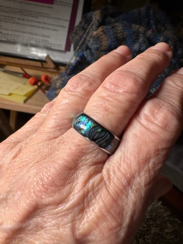 A reviewer's hand wearing the Nerium ring, showing the iridescent, colorful abalone inlay.