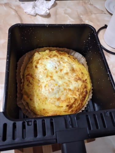 Recenzent prezentând un preparat auriu, copt, în cuva air fryer-ului Novio StonePro.