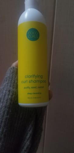 A reviewer holds up the yellow bottle of Clarifying Curl Shampoo.