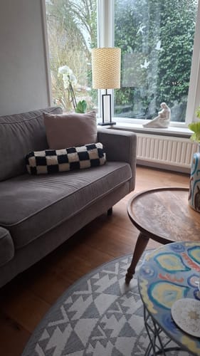 Recensent toont het geblokte HKliving Statement sierkussen op een grijze bank in een woonkamer.