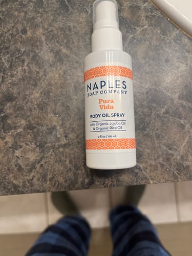 Reviewer's Pura Vida Luxe Body Oil Spray bottle on a dark marbled countertop.