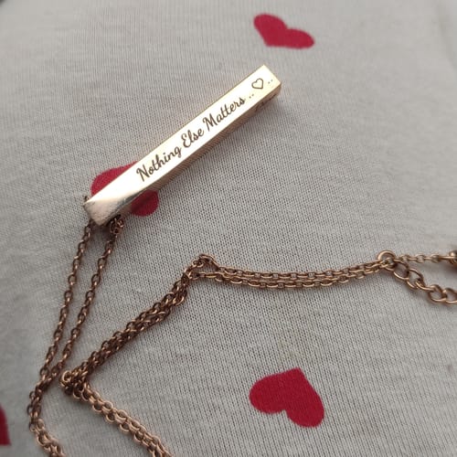Close-up of a customer's gold-colored Imperium bracelet, showing the bar pendant engraved with 'Nothing Else Matters ..' and a heart.