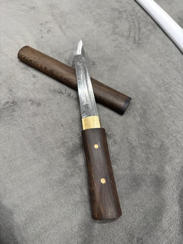 Customer's Tanto knife with its dark rosewood handle and matching scabbard resting on a grey, textured surface.