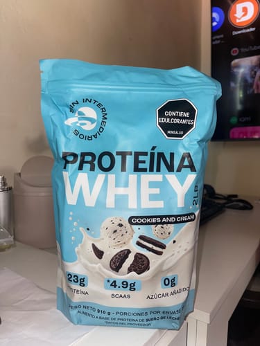 Un reseñador muestra el empaque azul de la Proteína Whey sabor Cookies and Cream sobre un escritorio.