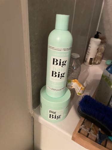 Une cliente montre le shampoing et le masque verts de la Gamme Résistance posés sur le rebord d'une baignoire.