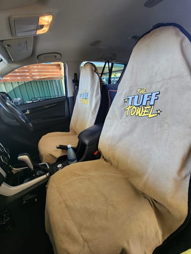 Reviewer's tan Waterproof Car Towel Seat Covers fitted on the two front seats of a vehicle, showing the logo.