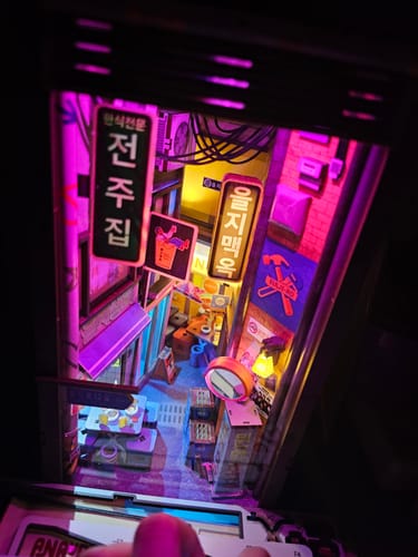 A reviewer's view of the finished Seoul Hipjiro Book Nook Kit, lit up to show a glowing cyberpunk alley.