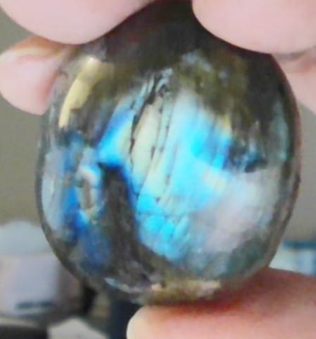 Close-up of a customer's hand holding a Labradorite Moonstone with a vibrant blue glow.