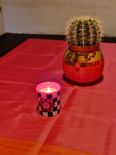 Kundenfoto der brennenden Sad Flower Statementkerze auf einem rosa Tisch neben einem Kaktus.