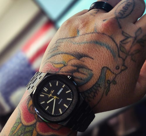 Reviewer's black Lucky Fours® Brone watch shown on their tattooed wrist.