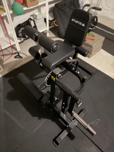 Rezensent zeigt den fertig montierten schwarzen Fullbody Multitrainer in einem Homegym auf einer Bodenmatte.