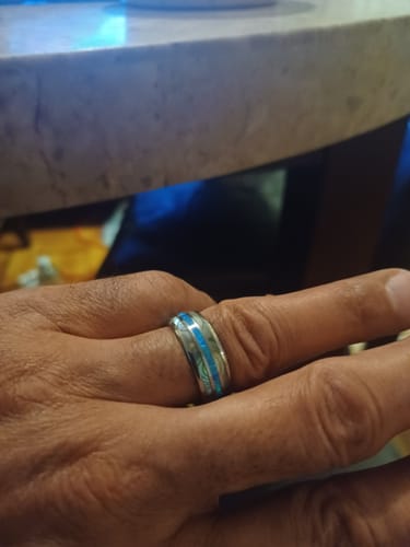 A customer's hand wearing the silver Vanguard ring, showing its bright blue opal and abalone inlay.