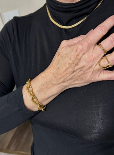 Customer wearing a gold necklace, bracelet, and rings from the WaterProof Jewelry Bundle against a black shirt.