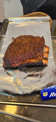 Un cliente muestra un rack de short rib cocido y sazonado sobre una hoja de papel de aluminio.