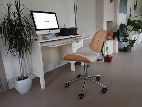 Klant's witte bureaustoel met houten rugleuning, geplaatst aan een bureau in een thuiskantoor.