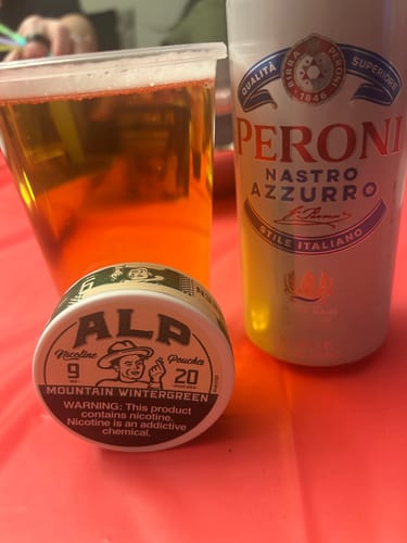 Customer's can of ALP Mountain Wintergreen Nicotine Pouches on a red table next to a beer, matching the review.