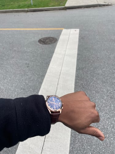 Customer wearing the Lucky Fours® Voyager watch with a brown leather strap and blue dial outdoors.