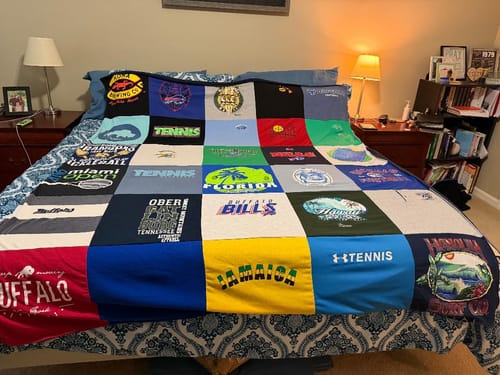 Customer's colorful Premium T Shirt Quilt made of many t-shirts spread neatly across a bed in a bedroom.