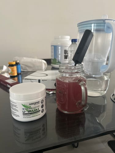 Customer's D-BLOAT container on a table next to a prepared red drink in a glass mug.