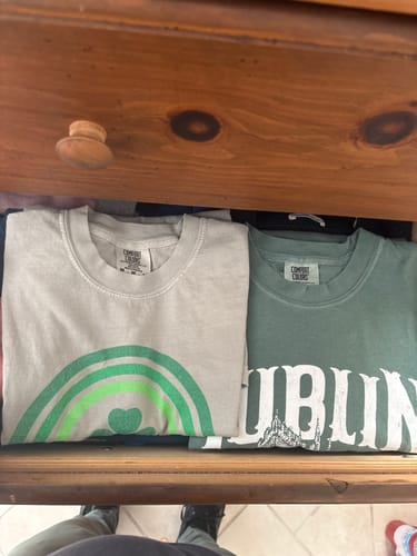 Customer's folded Ireland Rainbow Shamrock T-Shirt in a wooden drawer next to another shirt.