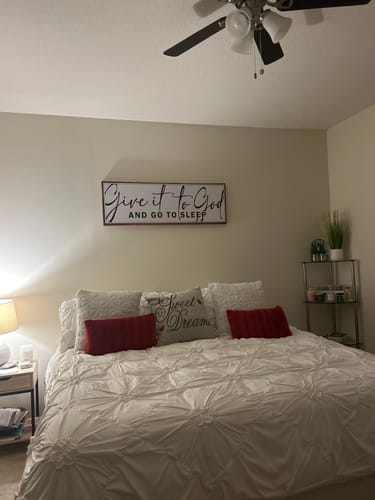 Customer's 'Give It To God And Go To Sleep' sign mounted on a bedroom wall above a neatly made bed.